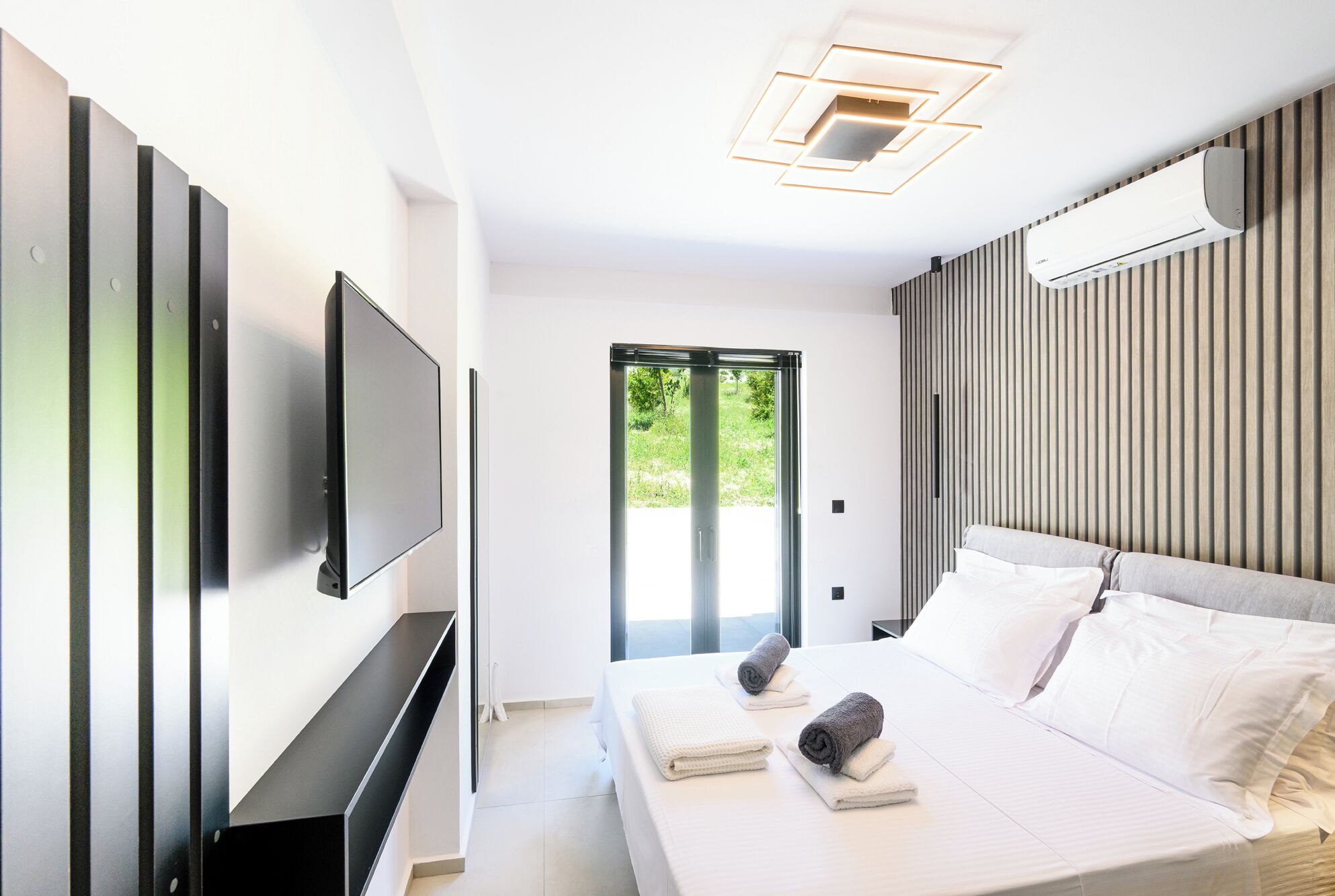 Una habitación de hotel moderna con una cama grande, un televisor de pantalla plana montado en la pared y una puerta corredera que da a un espacio al aire libre.