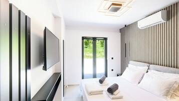 Una habitación de hotel moderna con una cama grande, un televisor de pantalla plana montado en la pared y una puerta corredera que da a un espacio al aire libre.