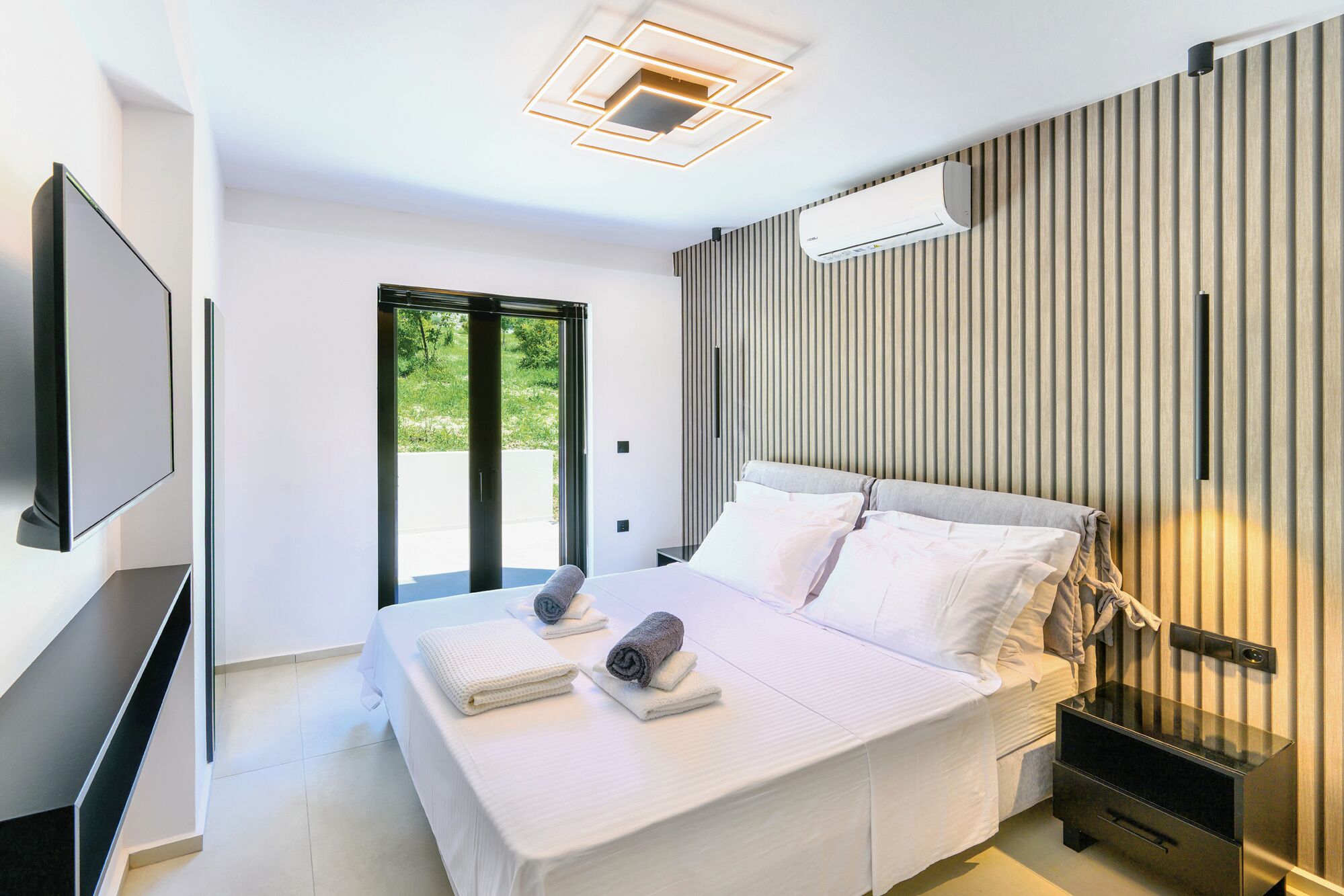 Un dormitorio moderno con cama, mesitas de noche, televisor de pantalla plana y un amplio ventanal.