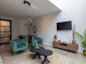 Un salon moderne avec des fauteuils turquoise, une table basse noire, un meuble en bois et un téléviseur fixé au mur.