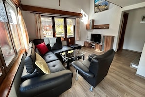 A modern living room with a black leather sofa, a glass coffee table, and a television.