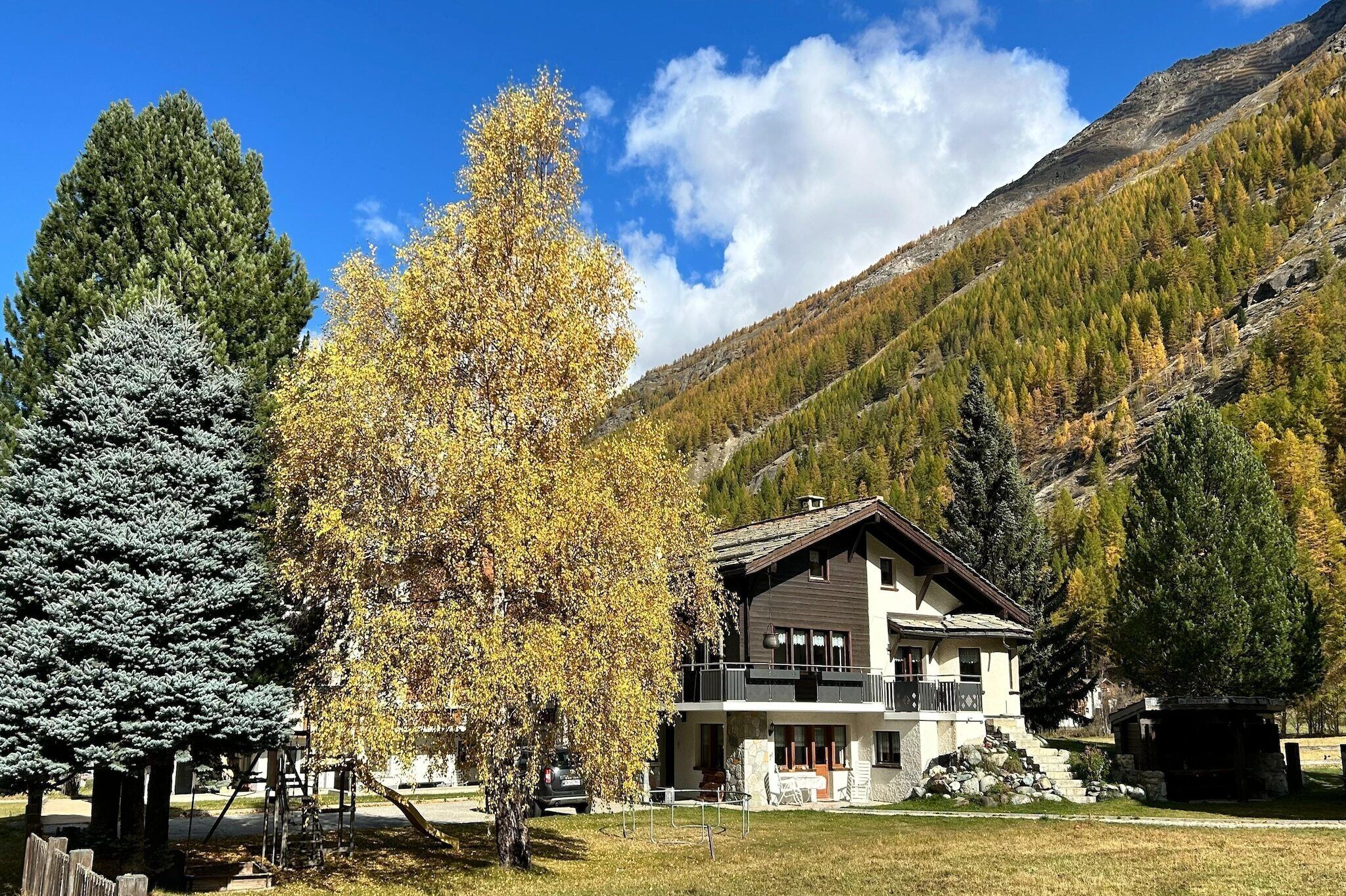 Eine zweistöckige Chalet mit Balkon, umgeben von Bäumen und Bergen.
