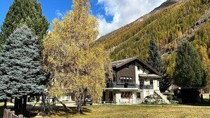 A two-story chalet with a balcony, surrounded by trees and mountains. - Chalet in Saas Fee near Ski Slopes (Saas Grund)