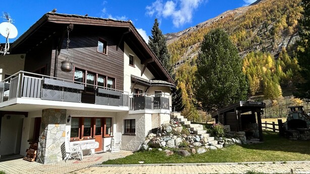 A chalet-style building with a stone facade, a balcony, and a stone staircase leading to a wooden deck. - Chalet in Saas Fee near Ski Slopes (Saas Grund)