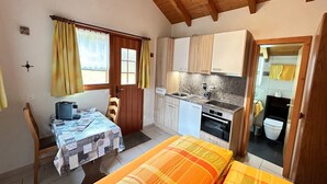 A compact room with a bed, a small table, a kitchenette, and a bathroom visible through an open door. - Chalet Stadel: Alpine Comfort (Saas Grund)