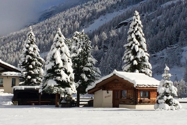 Ein mit Schnee bedecktes Blockhaus mit Holzfassade, umgeben von schneebedeckten BĂ€umen und einer Bergkulisse.