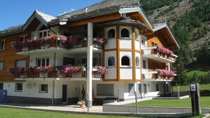 Un hôtel à plusieurs étages, doté de balcons ornés de fleurs, qui se dresse sur un fond de montagnes.