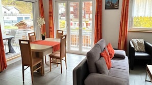 Une pièce comprenant une table à manger, des chaises, un canapé et une fenêtre avec des rideaux.