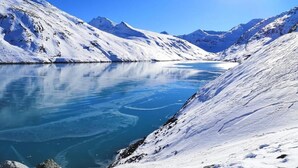 Un paysage montagneux enneigé, avec un lac d’un bleu profond qui reflète le ciel.
