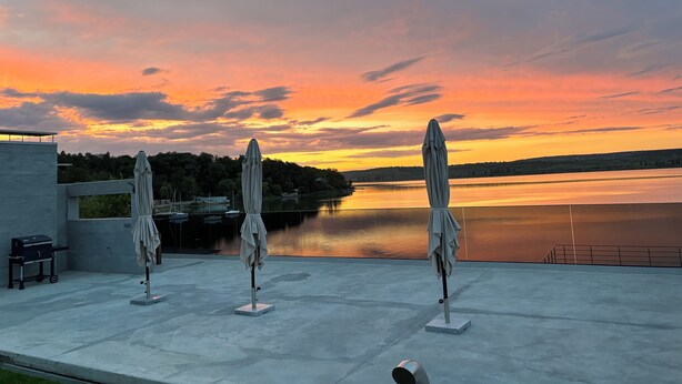 An outdoor terrace with three umbrellas, a grill, and a view of a lake at sunset. - Plein Air Residence & Resort (Vatra)