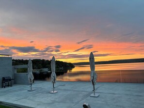 An outdoor terrace with three umbrellas, a grill, and a view of a lake at sunset. - Plein Air Residence & Resort (Vatra)