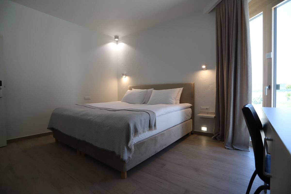 Un dormitorio con cama, mesitas de noche, escritorio y ventana con cortinas.