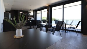 A modern dining area with a dark wooden table, white vase with green plants, and black chairs. Large windows offer a view of the outdoors. - Plein Air Residence & Resort (Vatra)