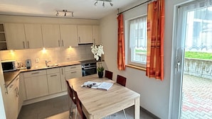 A kitchen with white cabinets, a dining table with chairs, a potted plant, and a window with curtains.