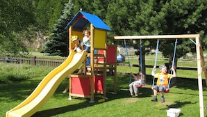 A playground with a yellow slide, a swing set, and a small wooden playhouse.
