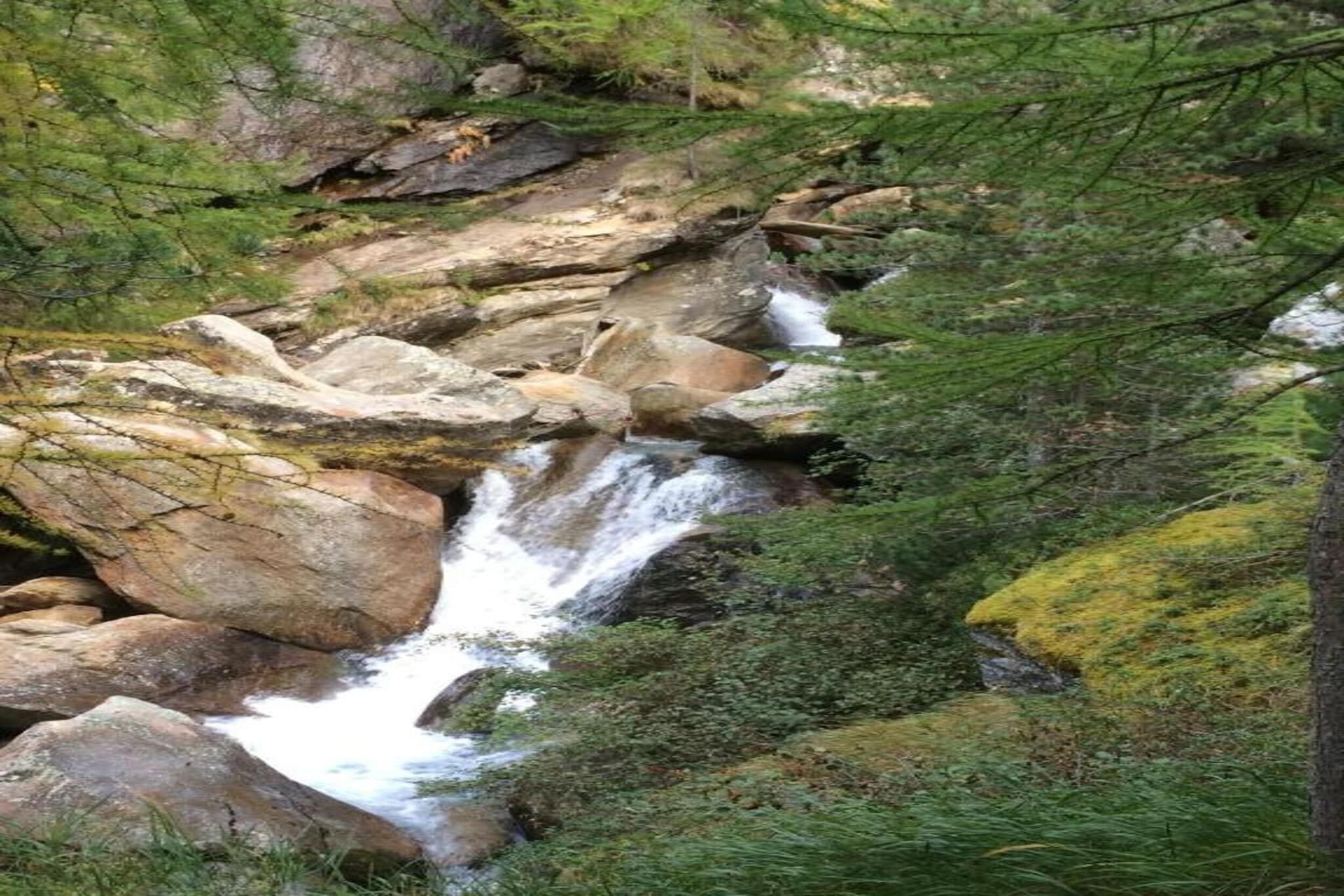 Een natuurlijke waterval, omringd door rotsen en groen.