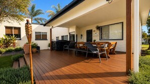A covered outdoor patio with wooden flooring, a barbecue grill, and outdoor seating. - Surfside - Beach Getaway (WOOLI)