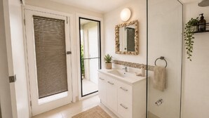 A bathroom with a white sink, a mirror, a towel rack, and a shower area. - Surfside - Beach Getaway (WOOLI)