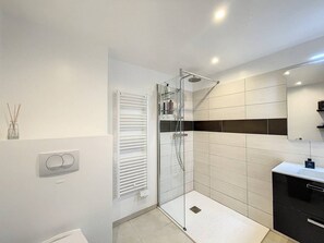 Une salle de bain moderne avec une douche à parois de verre, des carreaux blancs, un meuble noir et un miroir au-dessus du lavabo.