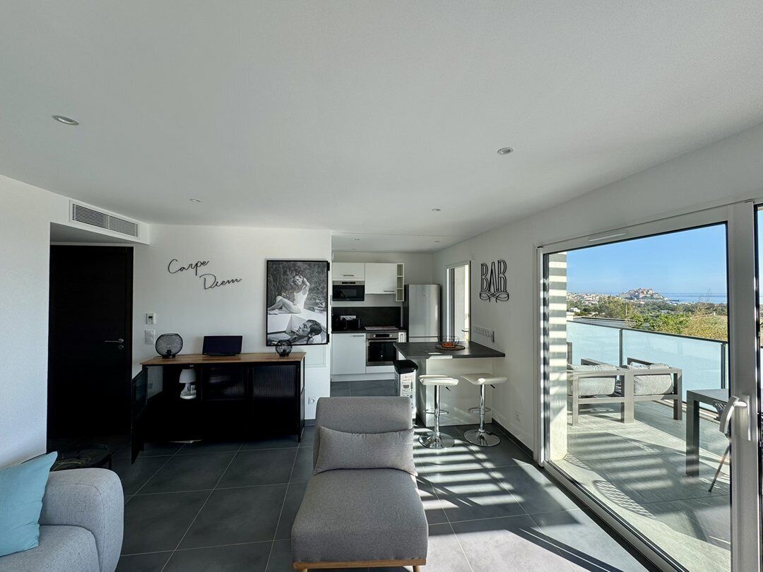 A modern apartment with a living area, kitchen, and balcony with a view.