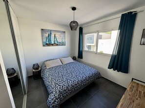 Une chambre à coucher avec un lit, un tableau, une fenêtre avec des rideaux et une table de chevet avec une lampe.