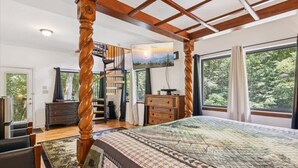 Un dormitorio amplio con una cama grande, vigas de madera en el techo, una escalera y vistas panorámicas por las ventanas.