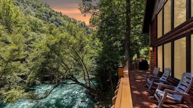 Una terraza de madera con mobiliario exterior con vistas a un río y zona boscosa.