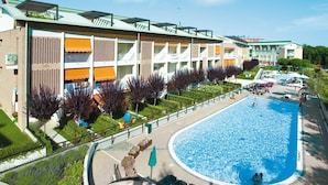 A hotel with a large swimming pool, multiple balconies, and a well-maintained garden area. - Enjoy you holiday by the pool with solarium (Bibione)