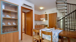A dining area with a wooden table and chairs, a kitchen in the background, and a staircase leading to an upper floor. - Enjoy you holiday by the pool with solarium (Bibione)
