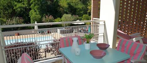 A balcony with a pool, outdoor seating, and a view of the pool area.