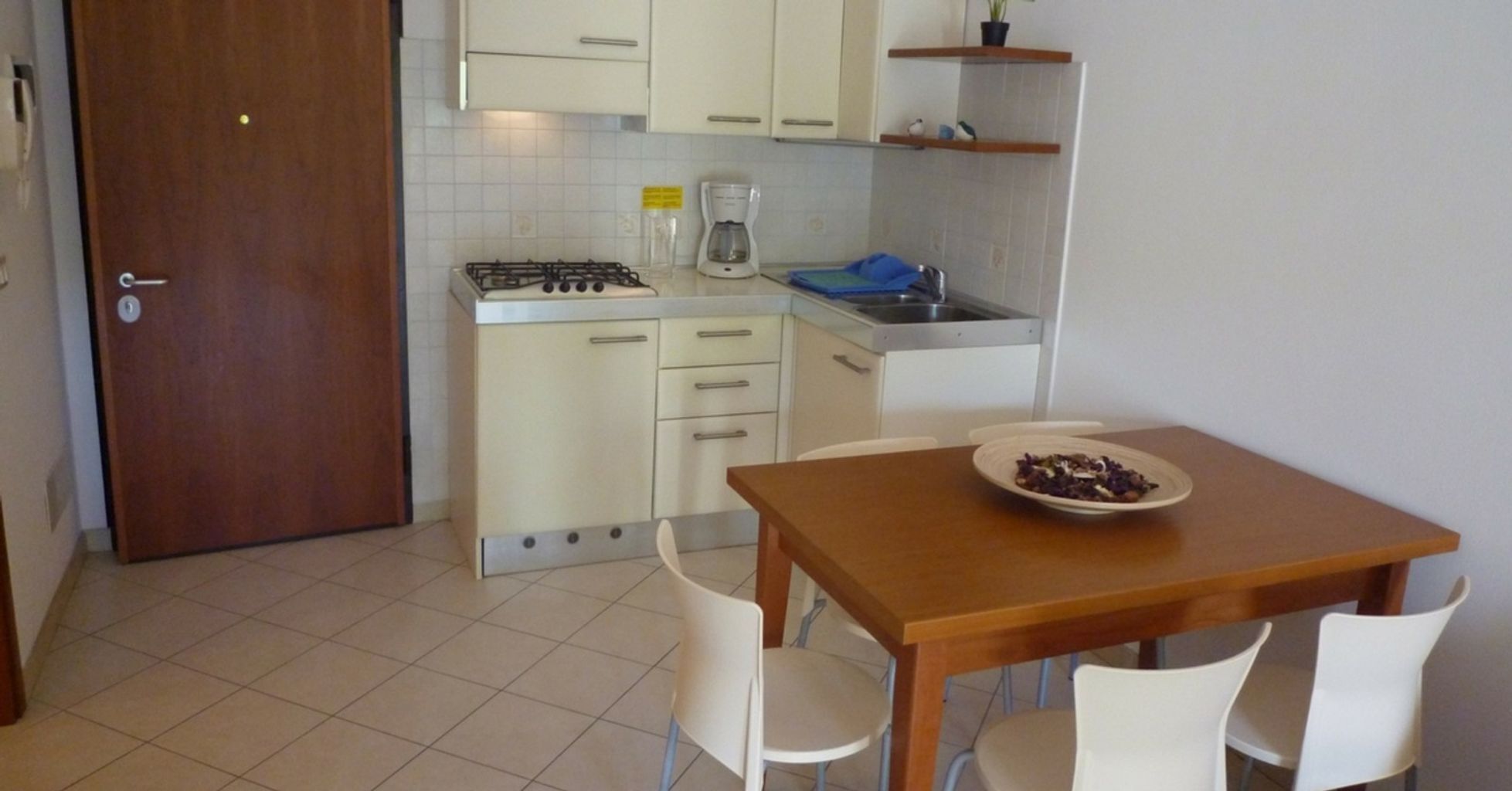 A compact kitchen with white cabinets, a gas stove, a coffee maker, and a dining table with chairs.