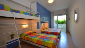 Ein Zimmer mit Etagenbetten, einem Schreibtisch und einem Stuhl. Ein Fenster mit Vorhängen bietet Blick auf Grünflächen.