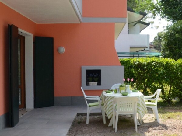 An outdoor patio with a table and chairs, a framed picture on the wall, and a door.