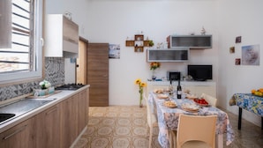 Una cucina compatta con zona pranzo, caratterizzata da pavimento piastrellato, mobili in legno, forno a incasso e un tavolo imbandito con piatti e un vaso di fiori.