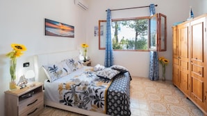 Una camera da letto con un letto, un comodino, un armadio, una finestra con tende e un quadro appeso al muro.