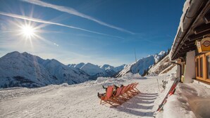 Pendio montuoso innevato con una fila di sedie da spiaggia a righe rosse e bianche e un paio di sci appoggiati a un edificio.