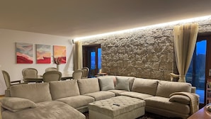 A living room with a sectional sofa, a dining table with chairs, and a stone accent wall.