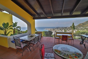 Una terraza con vistas al mar, con mobiliario exterior y plantas en macetas.
