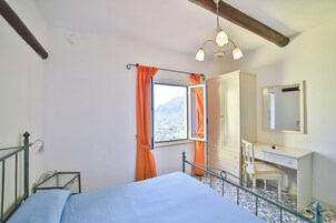 Un dormitorio con cama, escritorio, silla, armario y ventana con cortinas.