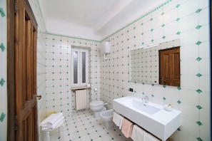 A bathroom with a white sink, toilet, and bidet, tiled floor, and a wooden door. - SWEETPOSEIDON (Forio)