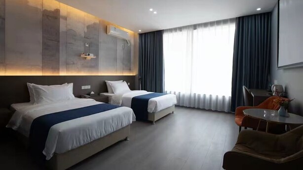 Une chambre d’hôtel avec deux lits, un bureau, une chaise et une grande fenêtre avec des rideaux.