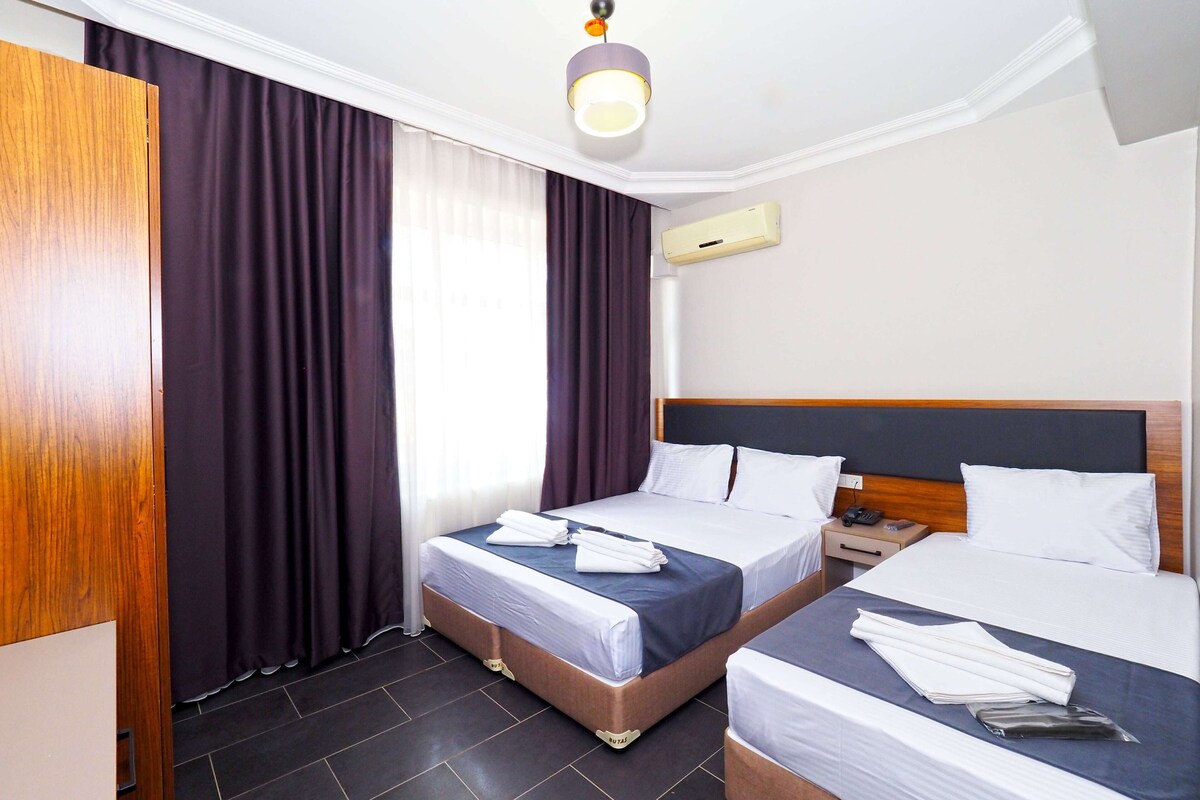 A hotel room with two beds, dark curtains, a ceiling light, and a wall-mounted air conditioner.