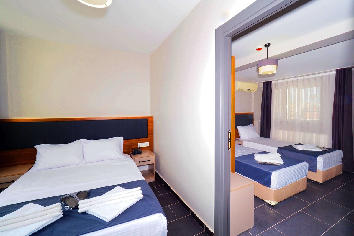 A hotel room with a large bed, two smaller beds, a bedside table, a mirror, and a ceiling light.