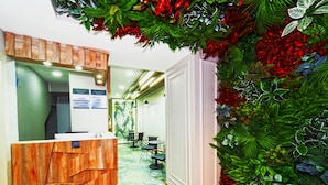 A reception area with a wooden desk labeled "RECEPTION," a sign indicating breakfast times, and a wall decorated with artificial plants and flowers. - Diamond Hotel Old City (Istanbul)