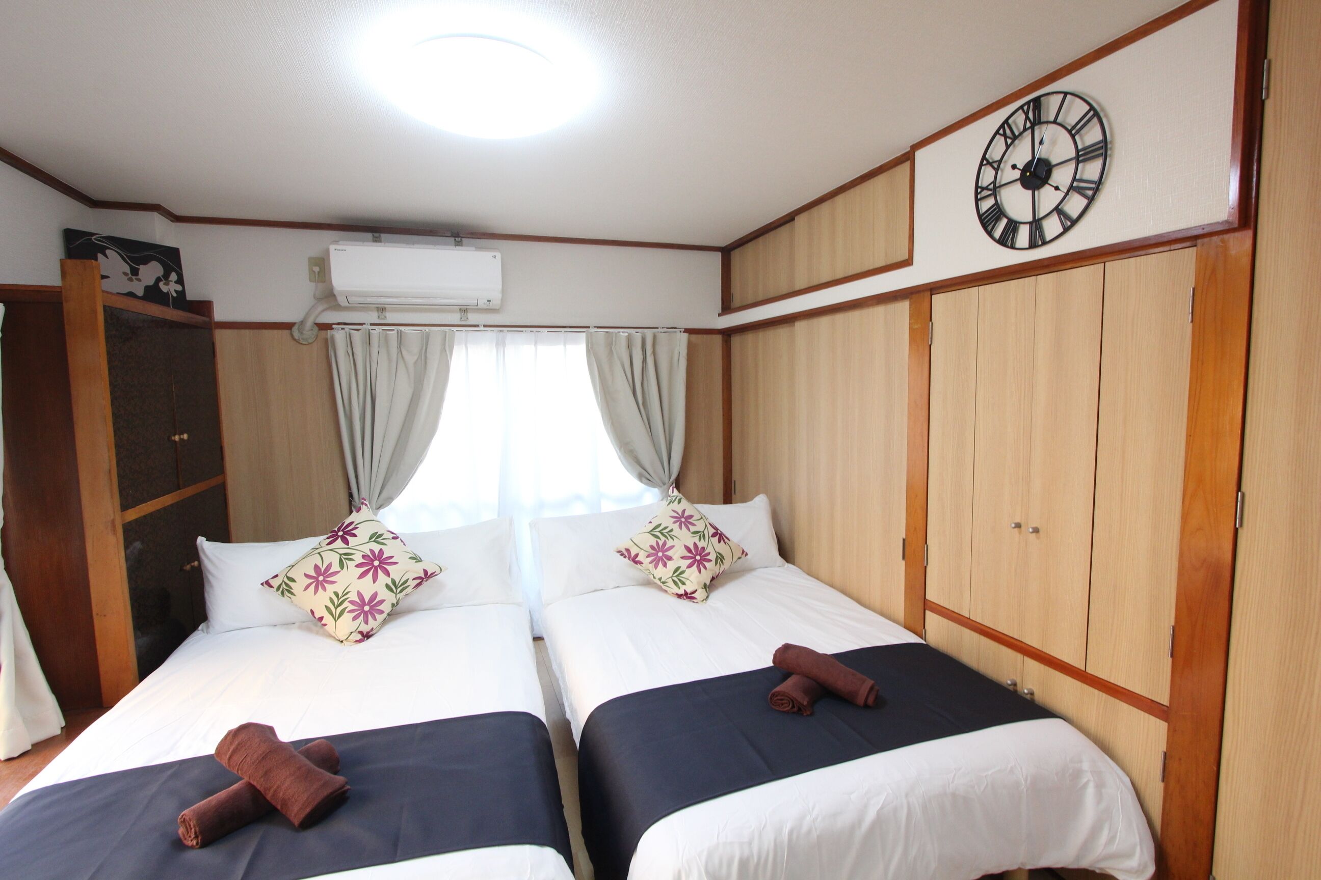 A hotel room with two beds, a clock on the wall, and an air conditioning unit.