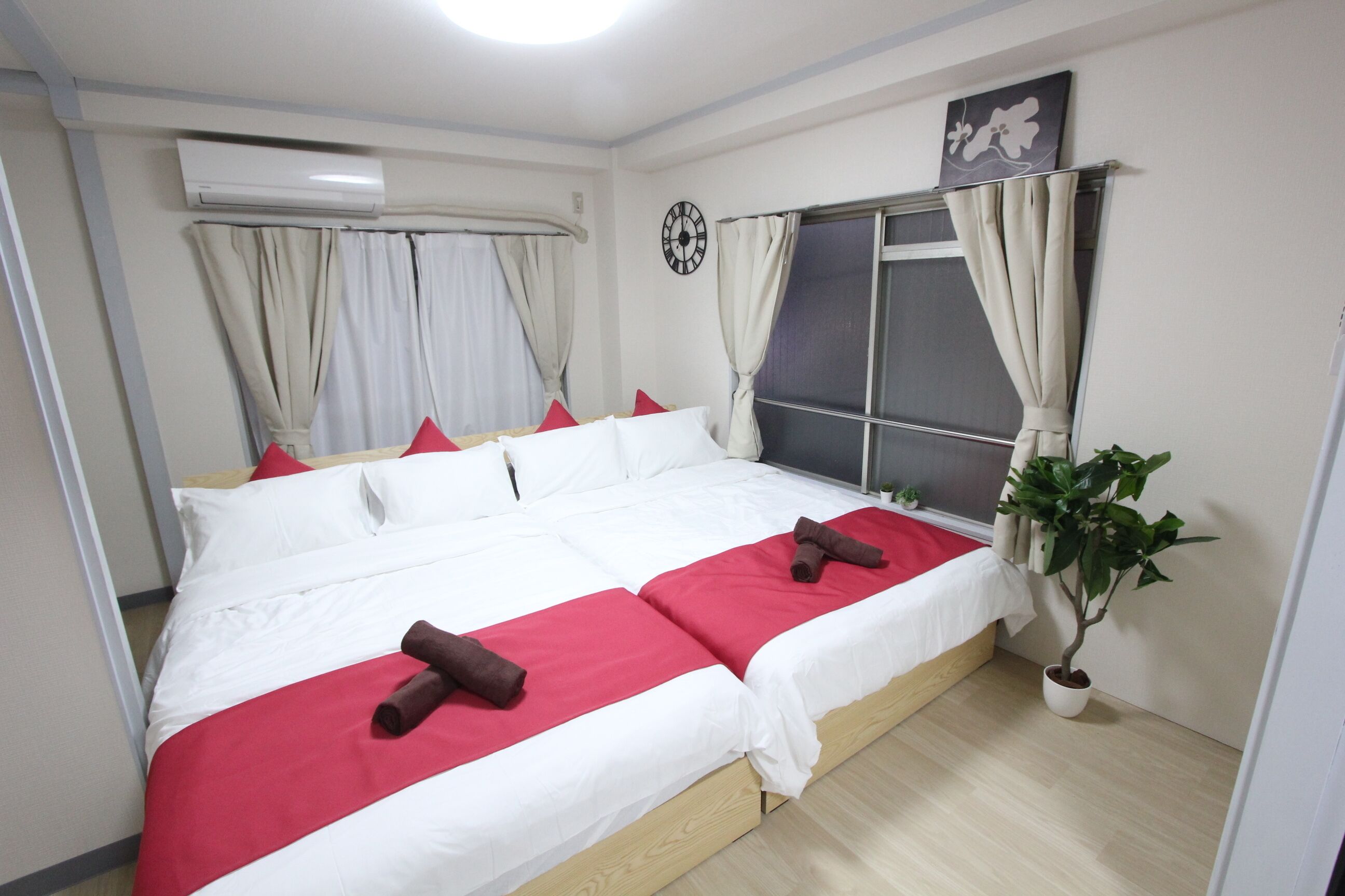 Una cama doble con ropa de cama roja y blanca, una planta en maceta y una ventana con cortinas.