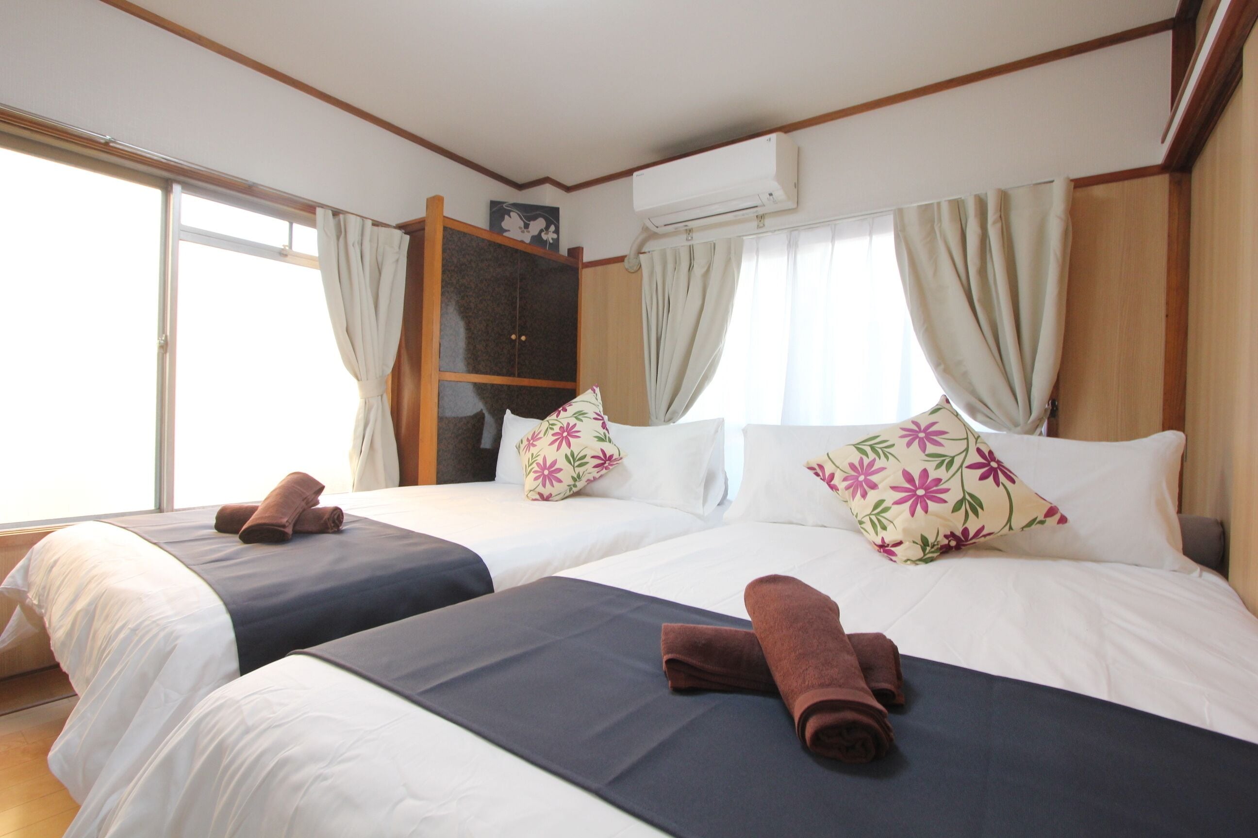 A hotel room with two beds, a wardrobe, and an air conditioning unit.