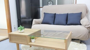 Een moderne woonkamer met een salontafel met glazen blad, een beige bank met blauwe kussens en een kleine plant in pot.
