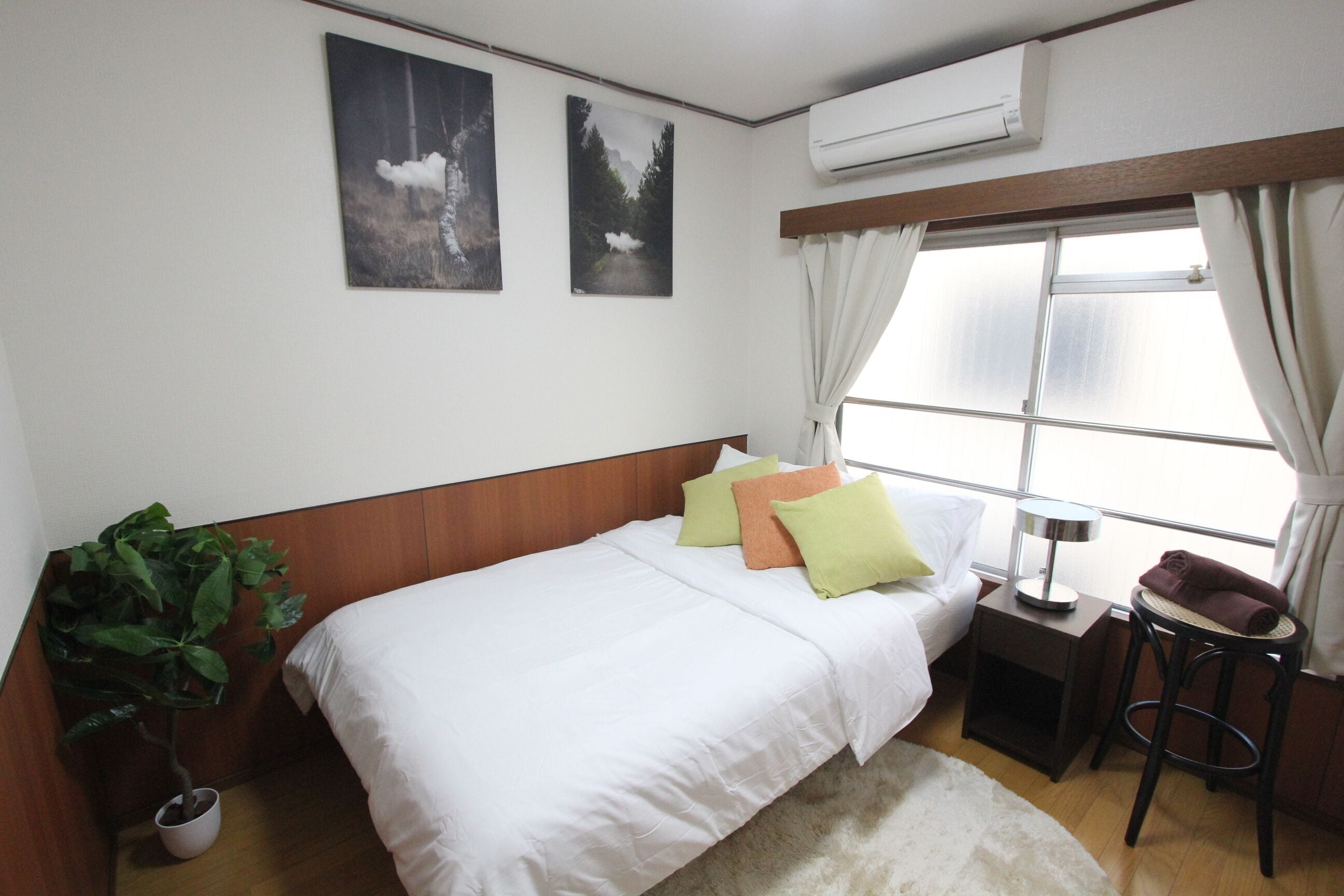 A hotel room with a bed, a nightstand, a potted plant, and a window with curtains.