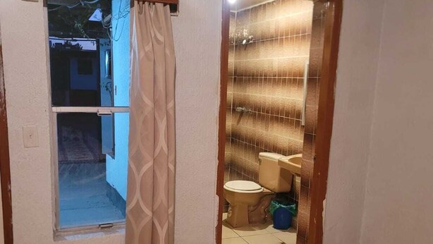 Casa de banho com sanita, chuveiro e janela com cortina.